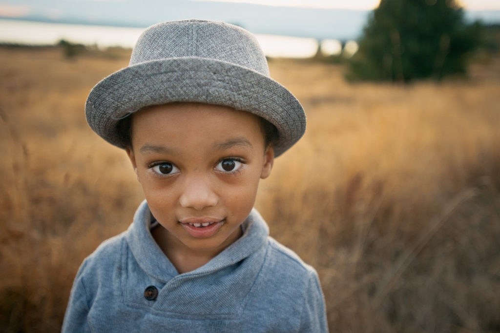 Little boy in a dapper hat standing in a field over looking Puget Sound